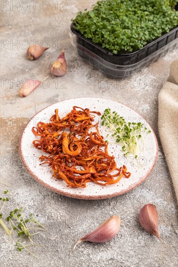 Fried Cordyceps militaris mushrooms on brown concrete background with microgreen, herbs and spices. Side view, copy space