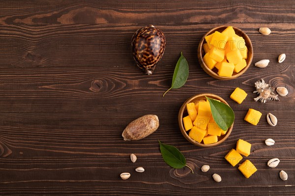Dried and candied mango cubes in wooden bowls on brown wooden textured background. Top view, flat lay, copy space, vegan, vegetarian food concept