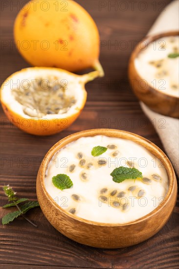 Yoghurt with granadilla and mint in wooden bowl on brown wooden background and linen textile. side view, close up, selective focus