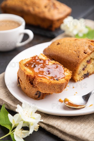 Homemade cake with raisins, almonds, soft caramel and a cup of coffee on a black concrete background and linen textile. Side view, close up, selective focus