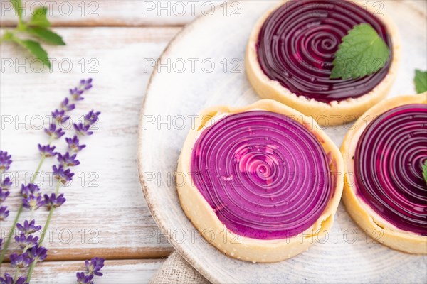 Sweet tartlets with jelly and milk cream with cup of coffee on a white wooden background and linen textile. Side view, close up, selective focus