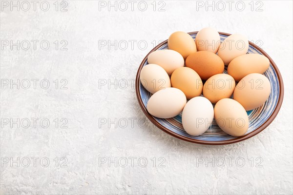 Pile of colored chicken eggs on plate on a gray concrete background. side view, copy space, close up