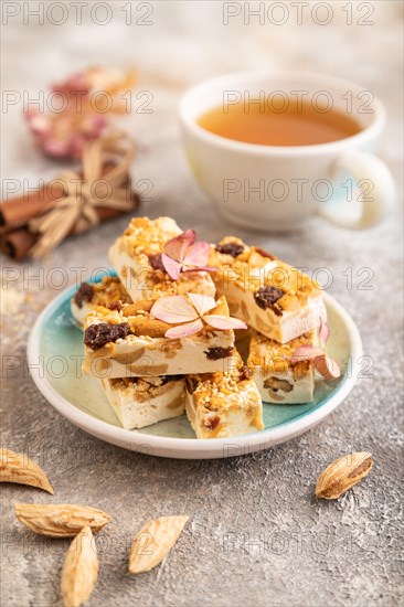 Traditional candy nougat with nuts and sesame with cup of green tea on brown concrete background. side view, close up, selective focus