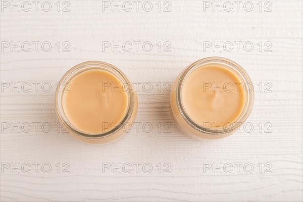 Baby puree with fruits mix, apple, banana infant formula in glass jar on white wooden background. Top view, flat lay, close up, artificial feeding concept