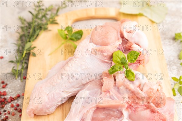 Raw turkey wing with herbs and spices on a wooden cutting board on a brown concrete background. Side view, close up, selective focus