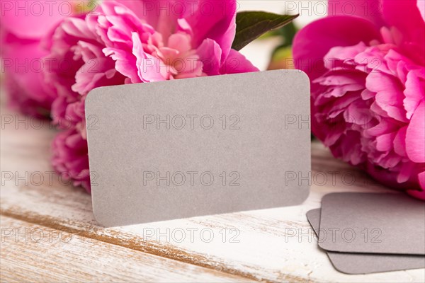Gray business card with pink peony flowers on white wooden background. side view, copy space, still life. Breakfast, morning, spring concept