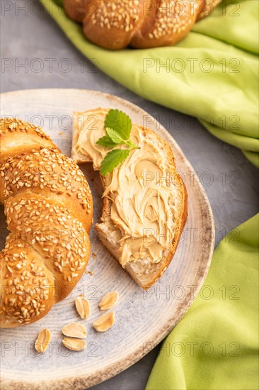 Homemade sweet bun with peanut butter and cup of coffee on a gray concrete background and green linen textile. side view, close up, selective focus