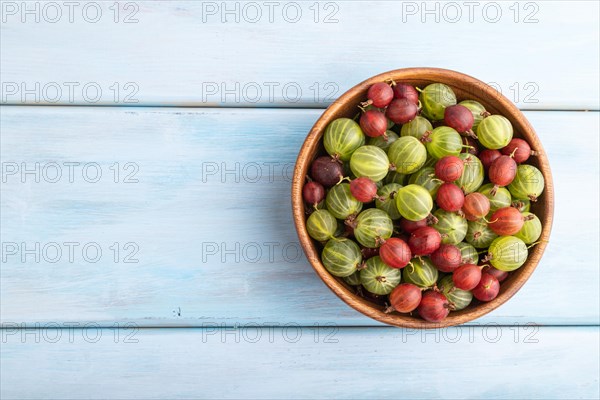 Fresh red and green gooseberry in wooden bowl on blue wooden background. top view, flat lay, copy space