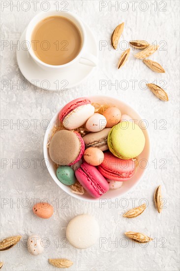 Multicolored macaroons and chocolate eggs in ceramic bowl, cup of coffee on gray concrete background. top view, close up, still life. Breakfast, morning, concept