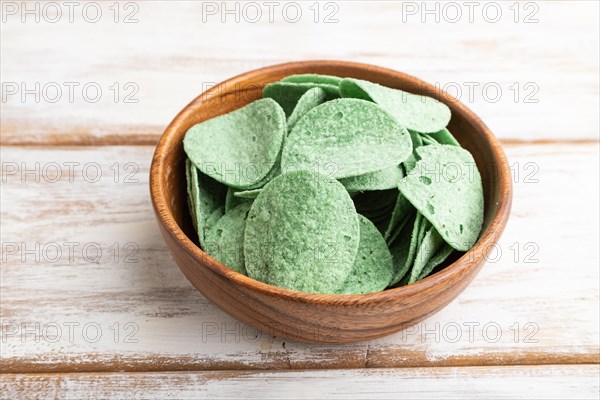 Green potato chips with herbs in wooden bowl on white wooden background. Side view, close up