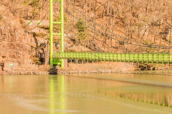 Green suspension bridge over a river with trees and brown grass in the background in South Korea
