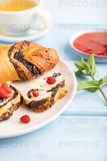 Homemade sweet bun with strawberry jam and cup of green tea on a blue wooden background. side view, close up, selective focus