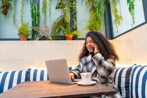 Casual young businesswoman with curly hair working in a colorful cafeteria drinking coffee