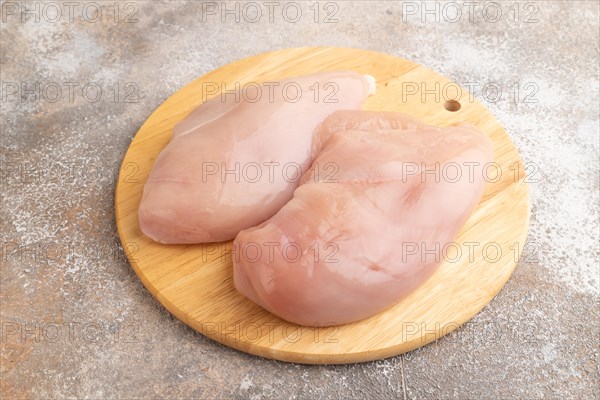 Raw chicken breast on a wooden cutting board on a brown concrete background. Side view, close up