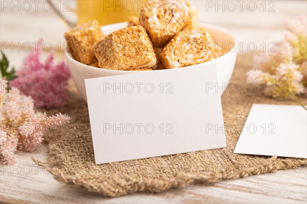 White business card with traditional turkish delight (rahat lokum) in white ceramic bowl on a white wooden background. side view, close up
