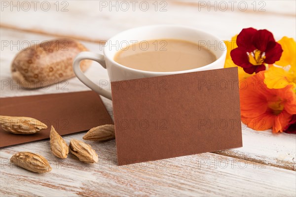 Brown paper business card mockup with orange nasturtium flower and cup of coffee on white wooden background. Blank, side view, copy space, still life. spring concept