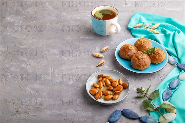 Homemade traditional turkish dessert sekerpare with almonds and honey, cup of green tea on gray concrete background and blue textile. side view, copy space