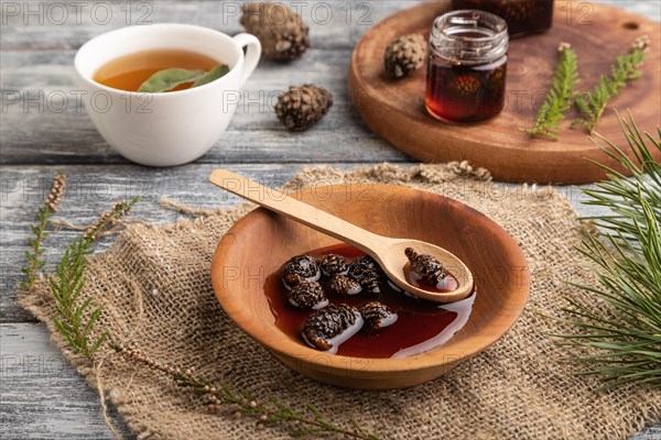 Pine cone jam with herbal tea on gray wooden background and linen textile. Side view, close up