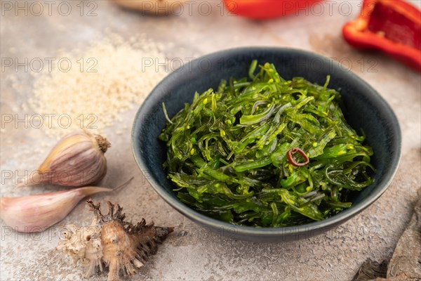 Chuka seaweed salad in blue ceramic bowl on brown concrete background. Side view, close up, selective focus