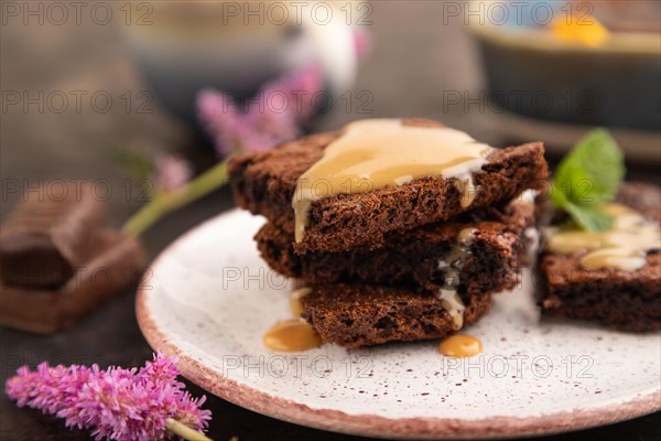 Chocolate brownie with caramel sauce with a cup of coffee on black concrete background. side view, close up, selective focus