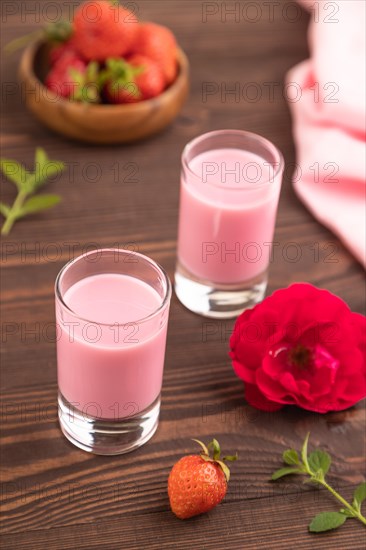 Sweet strawberry liqueur in glass on a brown wooden background and pink textile. side view, close up, selective focus