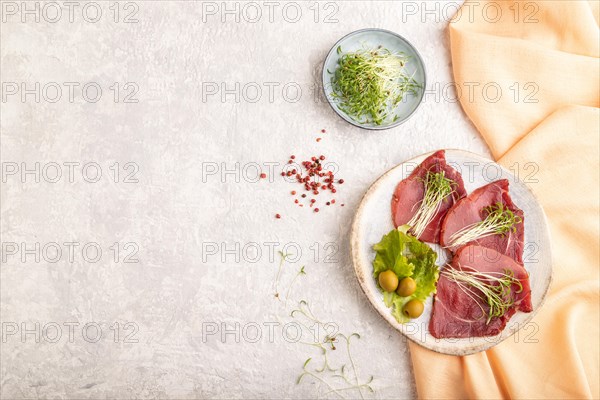 Slices of smoked salted meat with cilantro microgreen on gray concrete background and orange textile. Top view, flat lay, copy space