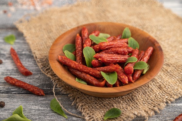 Small smoked sausage with borage microgreen, salt and pepper on gray wooden background and linen textile. Side view, close up, selective focus