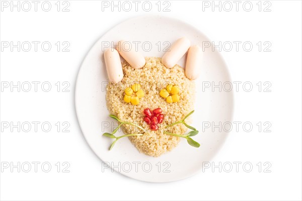 Funny mixed quinoa porridge, sweet corn, pomegranate seeds and small sausages in form of cat face isolated on white background. Top view, flat lay, close up. Food for children, healthy food concept