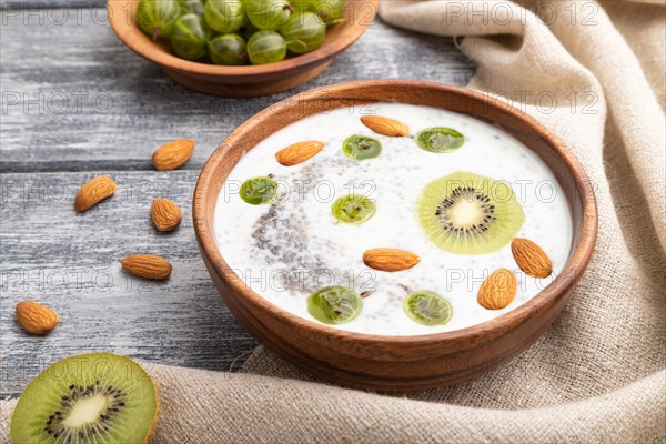 Yogurt with kiwi, gooseberry, chia and almonds in wooden bowl on gray wooden background and linen textile. Side view, close up