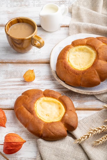 Sour cream bun with cup of coffee on a white wooden background and linen textile. Side view, close up