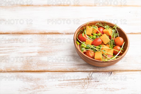 Vegetarian vegetable salad of tomatoes, pumpkin, microgreen pea sprouts on white wooden background. Side view, copy space, close up
