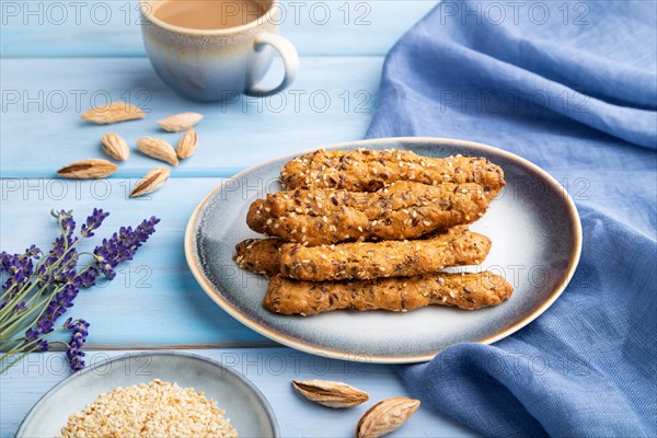 Crumble cookies with seasme and almonds on ceramic plate with cup of coffee and blue linen textile on blue wooden background. side view, close up