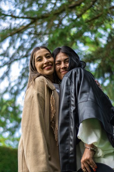 Vertical image of two female friends together happily looking at the camera with tree branches behind them
