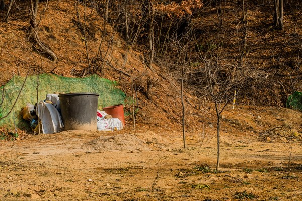 Daejeon, South Korea, January 24, 2020: Two large brown plastic tubs next to bags of fertilizer in field of young trees in wilderness. For editorial use only, Asia
