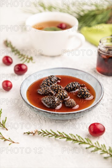 Pine cone jam with herbal tea on gray concrete background and green linen textile. Side view, selective focus