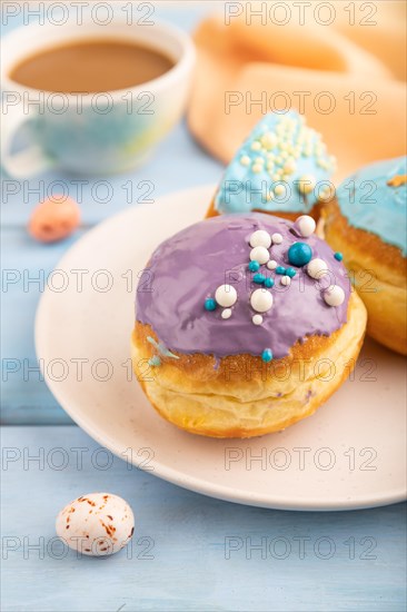 Purple and blue glazed donut and cup of coffee on blue wooden background and orange linen textile. side view, selective focus. Breakfast, morning, concept