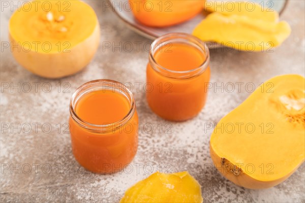 Baby puree with fruits mix, pumpkin, persimmon, mango infant formula in glass jar on brown concrete background. Side view, close up, selective focus, artificial feeding concept