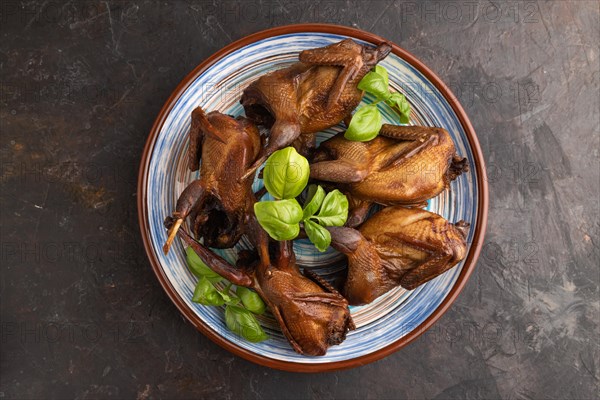 Smoked quails with herbs and spices on a ceramic plate on a black concrete background. Top view, flat lay, close up