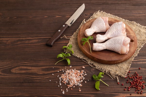 Raw chicken legs with herbs and spices on a wooden cutting board on a brown wooden background and linen textile. Side view, copy space