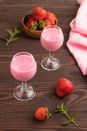 Sweet strawberry liqueur in glass on a brown wooden background and pink textile. side view, close up