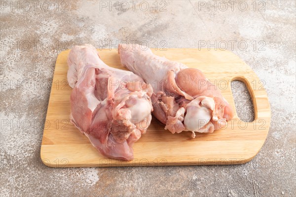 Raw turkey wing with herbs and spices on a wooden cutting board on a brown concrete background. Side view, close up