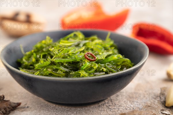 Chuka seaweed salad in blue ceramic bowl on brown concrete background. Side view, close up, selective focus