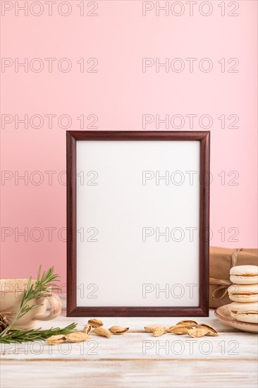 Brown wooden frame mockup with cup of coffee, almonds and macaroons on pink pastel background. Blank, side view, still life