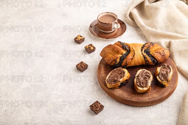 Homemade sweet bun with chocolate cream and cup of coffee on a gray concrete background and linen textile. side view, copy space