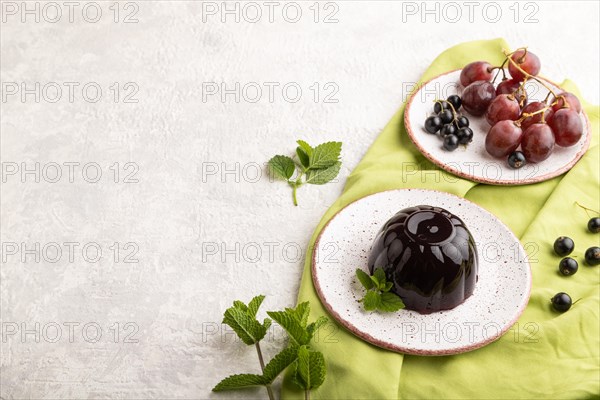Black currant and grapes jelly on gray concrete background and green linen textile. side view, copy space