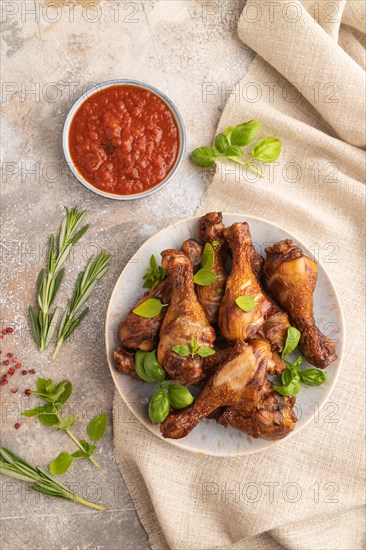 Smoked chicken legs with herbs and spices on a ceramic plate with linen textile on a brown concrete background. Top view, flat lay, close up