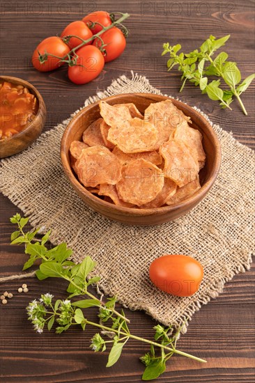 Slices of dehydrated salted meat chips with herbs and spices on brown wooden background and linen textile. Side view, close up