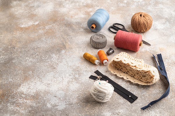 Sewing accessories: scissors, thread, thimbles, braid on brown concrete background. Side view, copy space