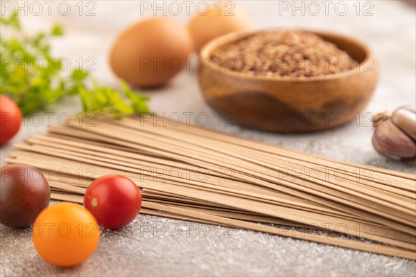 Japanese buckwheat soba noodles with tomato, eggs, spices, herbs on brown concrete background. Side view, close up, selective focus