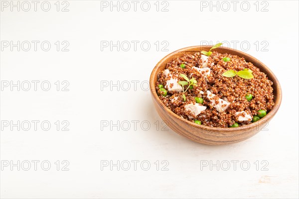 Quinoa porridge with green pea and chicken in wooden bowl on a white wooden background. Side view, close up, copy space